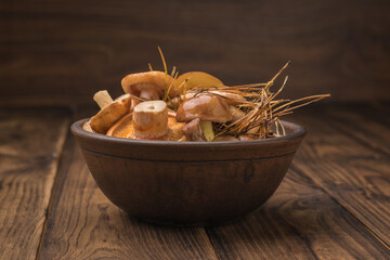 A deep clay bowl with wild mushrooms on a wooden table.