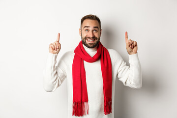 Christmas shopping and winter holidays concept. Happy bearded man in red scarf pointing fingers up, looking excited at copy space, standing over white background - Powered by Adobe