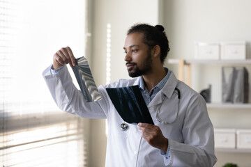 Serious young African American doctor examining radiography screening films of bones. Surgeon, radiologist reviewing xray scan of patient organs. Medical checkup, healthcare, radiology concept - obrazy, fototapety, plakaty