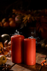 There are red candles on the wooden table. Smoke is coming from the newly extinguished wicks.