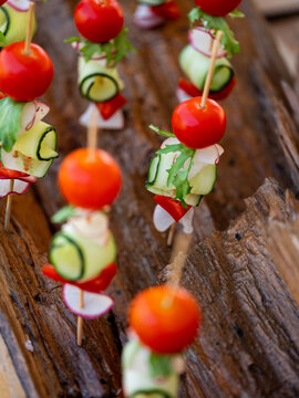 Healthy salad with vegetables tomatoes, cucumbers and greens on small sticks for picnic. Close up, selective focus, side view