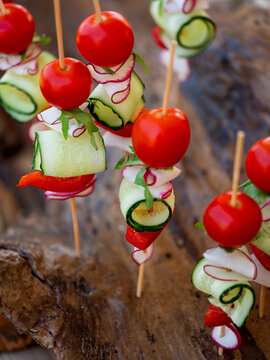 Small fresh snacks or  finger food with vegetables tomatoes, cucumbers and greens on small sticks for picnic. Close up, selective focus, side view