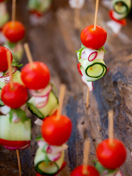 Vegetarian fresh snacks for picnic with vegetables tomatoes, cucumbers and greens on small sticks. Close up, selective focus, side view