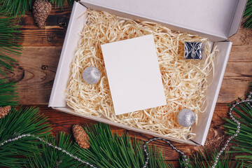 Merry Christmas, Happy New Year present box, paper sheet mock up, festive card template. Pine branches, cones, silver beads frame on wooden background.
