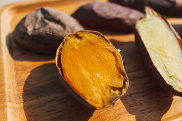 Cooked sweet potato cut into half on wooden plate.