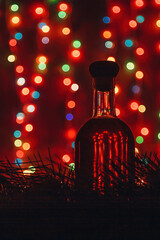 Old cellar alcohol drink bottle silhouette on red blurry Christmas background, shiny garland lights bokeh. Vertical shot, copy space.