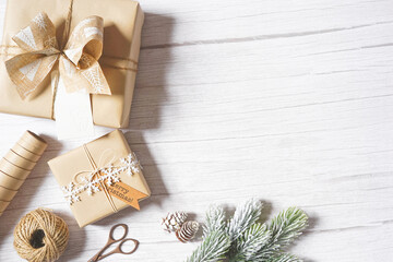 Christmas composition with presents, natural paper, branches, twine on white wooden background. Holiday craft gift wrapping. Merry Christmas greetings. Empty space for text. Copy space.