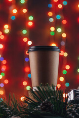 Disposable coffee cup on Christmas blurry background. Festive shiny garland lights bokeh, New Year hot beverages for walk. Vertical shot