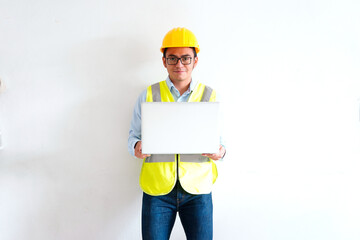 Young Latino contractor typing on his laptop on a white background with copy space, dressed in construction safety gear, horizontal photograph.