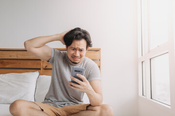 Sad Asian man has bad online chat news and feels disappointed on the smartphone.