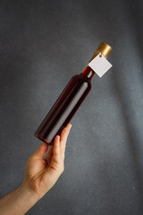 Male hand holding bottle of red wine, natural fruit alcohol liquor with empty label on grey background. Mock up, template for brand, vertical shot