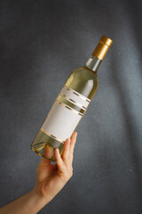 Male hand holding bottle of white dry or semi-sweet wine with white empty label on grey background. Mock up for brand, vertical shot