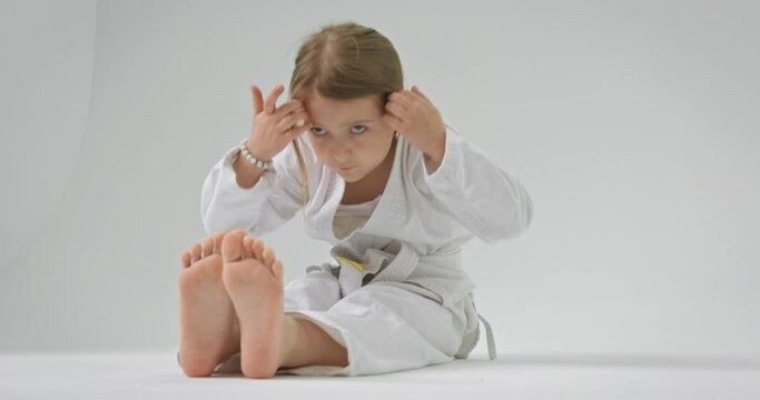 The girl sits on the floor with her legs straight and pulls her fingers to her toes.