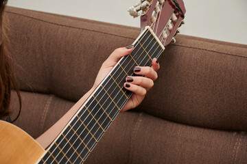 Small woman's hand holding a large brown guitar giving melodic tone with black painted nails