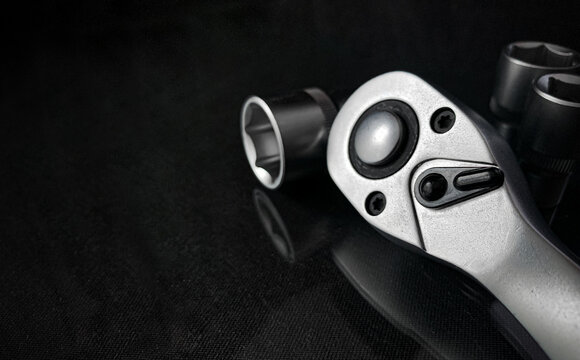 Ratchet wrench. Set of stainless steel hex sockets on shiny black surface. Universal professional tool for car repair. Low key photo.