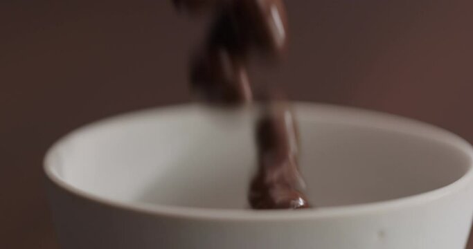 Slow motion pour chocolate covered pistachios in white bowl on walnut table