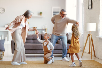 Active senior grandparents dancing with two happy kids grandchildren in living room