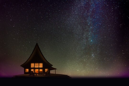 Silhouette of a cozy cabin at night overseeing Lake Superior, Upper Peninsula, Michigan, pictured against the stars of our galaxy and the earliest rays of sunrise