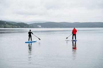 Two men stand and swim on sup boards on the lake on a cloudy day. Active rest on the lake with friends.