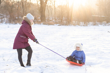 Sledding at winter time, mother carries daughter on a on ice sled