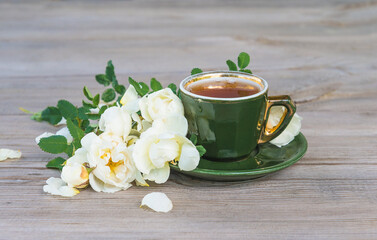 Coffee break in retro style; vintage cup of coffee and twig of white wild rose on rustic wooden background