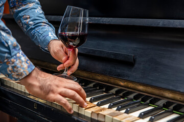 Old classical piano keys and Wine glass. a glass of red burgundy wine in an elegant etched wine glass resting on a piano keyboard.