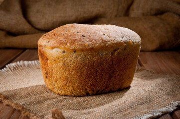 A loaf of delicious white bread made from natural products, on hops with flax saturation, without baker's yeast, on a wooden table surface.