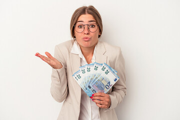 Young Russian business woman holding banknotes isolated on white background shrugs shoulders and open eyes confused.