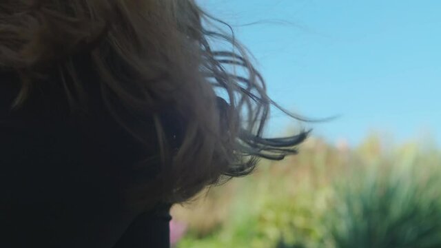 Girl's curly hair fluttering in the wind. Blurred trees and blue cky background