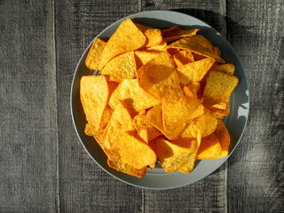 on the right, on a gray plate on a wooden background, there are many triangular corn tortilla chips. mexican cuisine. top view