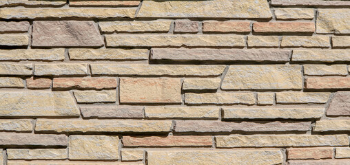 Sandstone building wall constructed in multi-colored, different sized stones in a pleasing horizontal pattern.