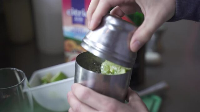 Slow motion view showing hands of bartender putting lime juice in metal shaker for making cocktail. Close up.
