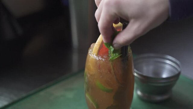 Close up of Bartender adding mint leaf on top of alcoholic Cynar Drink in glass at party,slow motion