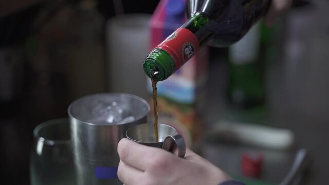 Close up view showing bartender pouring liquor in jigger and mixing it with ice in metallic shaker. Slow motion.