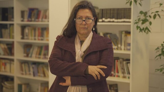 Middle aged woman standing in library and staring at the camera.