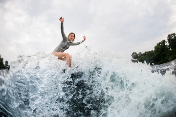 magnificent view on splashing wave and active woman on wakesurf rides down on it