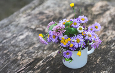 multi-colored flowers are in an iron mug, the mug is on a wooden surface