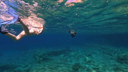 Underwater split photo of unidentified woman snorkeling in volcanic white rock caves with emerald clear sea