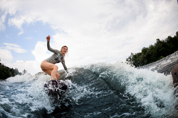 smiling young blonde woman on wakeboard rides down on big water wave.