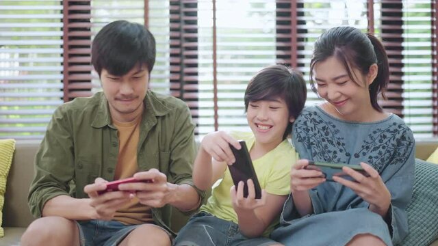 family quality time,asian parent and son sit relax playing game console or smart together laugh joyful smiling on sofa couch in living room at home,asian family homs isolation quarantine ideas concept