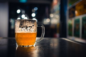Cold beer glass on a bar or pub desk, half empty. Tasty fresh yellow beer of Czech Republic. Dark pub on background.