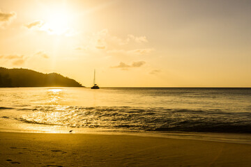 Coral sandy beach in the sunset light. In the distance a sailing yacht.