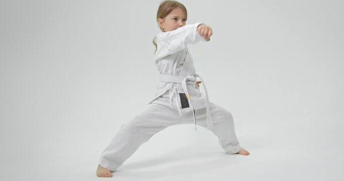 The child spreads his legs wide and strikes with straight hands in front of her. Karate exercises.