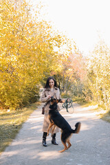 A smiling happy young woman in a coat walks with her dog pet trains and teaches puppy commands in an autumn park in nature in fall outdoor, selective focus