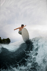 beautiful view on splashing wave and sportive man skilfully jumping on wakesurf board over it