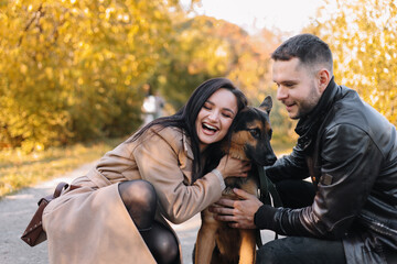 Happy young family a man and a woman in love have fun walking with their dog pet in a fall park in nature in autumn outdoor, selective focus