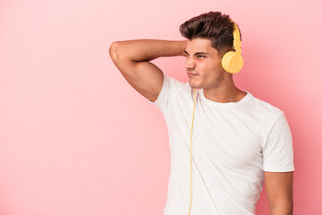 Young caucasian man listening to music isolated on pink background touching back of head, thinking...