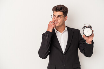 Young business caucasian man holding alarm clock isolated on white background relaxed thinking about something looking at a copy space.