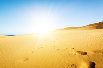 Fototapeta na wymiar Blue sky and sand dunes with footprints.