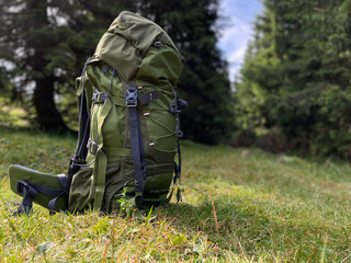 Hiker tourist green backpack on background green grass nature in  the forest, traveler relax holiday concept, travel adventure